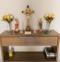 a wooden table topped with glass vases filled with flowers and figurines next to a crucifix