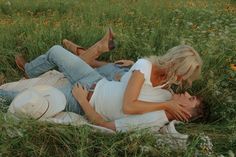 a man and woman laying in the grass with their arms around each other as they cuddle