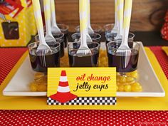 there are many cups and spoons on the plate with candy in them, as well as a sign that says oil change jelly cups