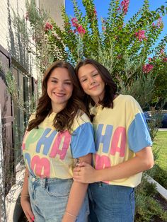 two young women standing next to each other in front of a fence with flowers on it