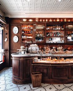 two people behind the bar in a fancy restaurant with lots of bottles and glasses on the shelves