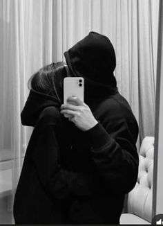 a person wearing a hoodie taking a selfie in front of a mirror with their cell phone