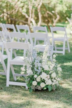 an arrangement of white flowers and greenery sits on the grass at this outdoor ceremony