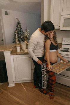 a pregnant woman holding a tray of cookies next to a man