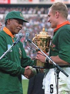 two men standing next to each other with microphones in front of them holding a trophy