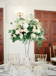 a vase filled with white flowers sitting on top of a table next to glasses and plates