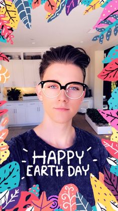 a young man wearing glasses and a happy earth day t - shirt in front of colorful leaves