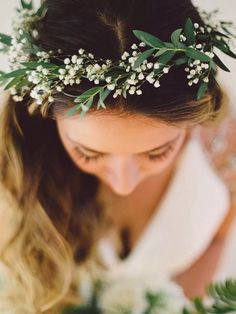 a woman wearing a flower crown with greenery on her head looking down at the ground