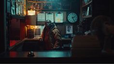 a man standing in front of a counter with clocks on the wall behind him and an alarm clock above his head