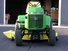 a green and yellow lawn mower parked in front of a garage with its door open