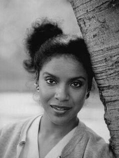 a black and white photo of a woman with an elephant trunk on her head, smiling at the camera