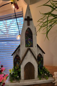 a white church with stained glass windows on top of a table next to a potted plant