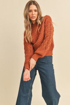 a woman in an orange sweater and jeans poses for the camera with her hand on her hip