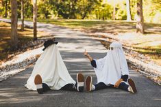 two people sitting on the side of a road with covers over their heads and feet