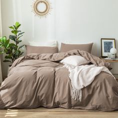 an unmade bed in a white room with a potted plant next to it