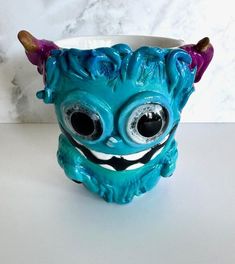 a blue ceramic cup with an evil looking face and horns on it's head