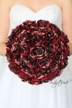 a woman in a white dress holding a red and black flowered bridal bouquet