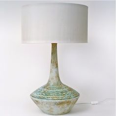 a ceramic lamp with a white shade on it and a cord plugged into the base