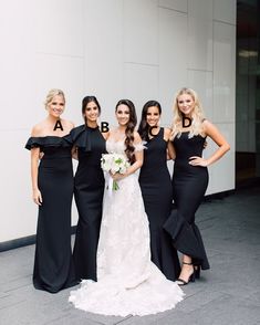 four bridesmaids in black dresses posing for a photo outside the building with their bouquets