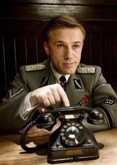 a man in uniform sitting at a table with an old phone