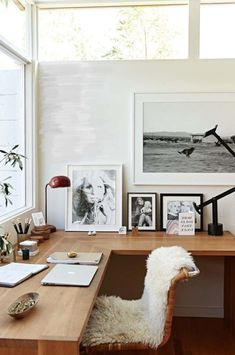 a desk with a chair and pictures on the wall next to it in front of a window