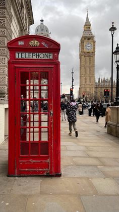 a red phone booth sitting on the side of a street next to a tall clock tower