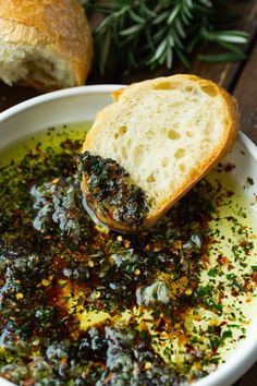 a white bowl filled with bread and pesto on top of a wooden table next to an open baguette