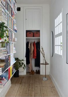 a white room with bookshelves and clothes hanging on the wall, in front of a wooden floor