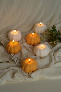 four pumpkin candles sitting on top of a white cloth