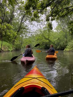 two people in kayaks paddling down a river surrounded by trees and greenery