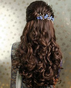 the back of a woman's head with long curly hair and blue flowers in her hair