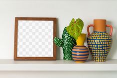 three colorful vases are on a shelf next to a wooden frame and a cactus