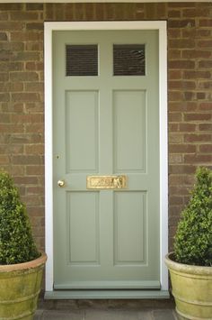 two potted plants next to a green door with gold lettering on the front and side