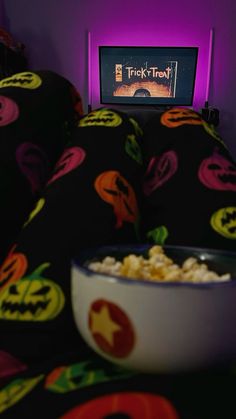 a bowl of popcorn sitting on top of a bed in front of a tv screen