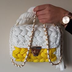 a woman's hand holding a white and yellow purse with braiding on it