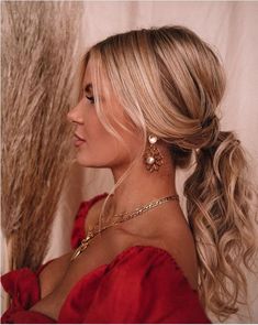 a woman with blonde hair wearing gold earrings and a red dress looking off to the side