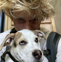 a young man with blonde hair holding a dog in his lap and looking at the camera