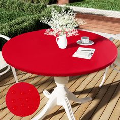 a red table and white chairs on a wooden deck with flowers in a vase next to it