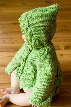 a baby sitting on the floor wearing a green knitted hoodie and matching shoes