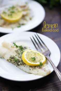 two white plates topped with fish covered in lemon and parsley next to a fork