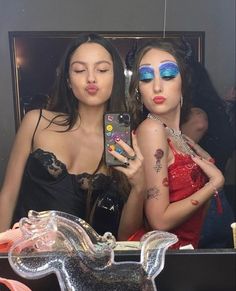 two beautiful women with makeup on their faces taking a selfie in front of a mirror