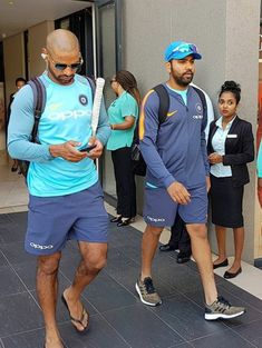 two men in blue shirts and shorts are looking at their cell phones while others watch