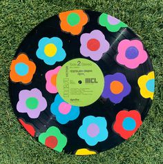 a black record with multicolored flowers on it sitting in the grass, next to a pair of scissors