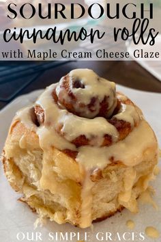 a cinnamon roll with maple cream cheese glaze is on a white plate and has the words sourdough cinnamon rolls over it