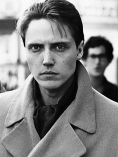 black and white photograph of man in trench coat looking at camera with other people behind him