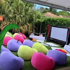 an outdoor party setup with bean bag chairs and large televisions on the lawn, surrounded by palm trees