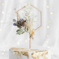 a white cake with gold leaf decoration and flowers on top is sitting on a table