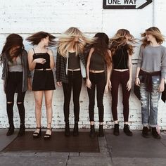 a group of girls standing in front of a white brick wall with their backs to the camera