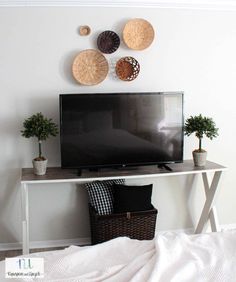 a flat screen tv sitting on top of a white table next to a basket filled with plants