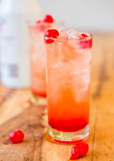 two glasses filled with ice and cherries on top of a wooden table